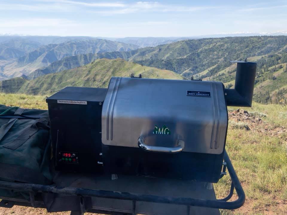 The Davy Crockett grill which is rated as one of the best pellet grills under $500 is shown at the top of a mountain with far reaching views of other mountains behind