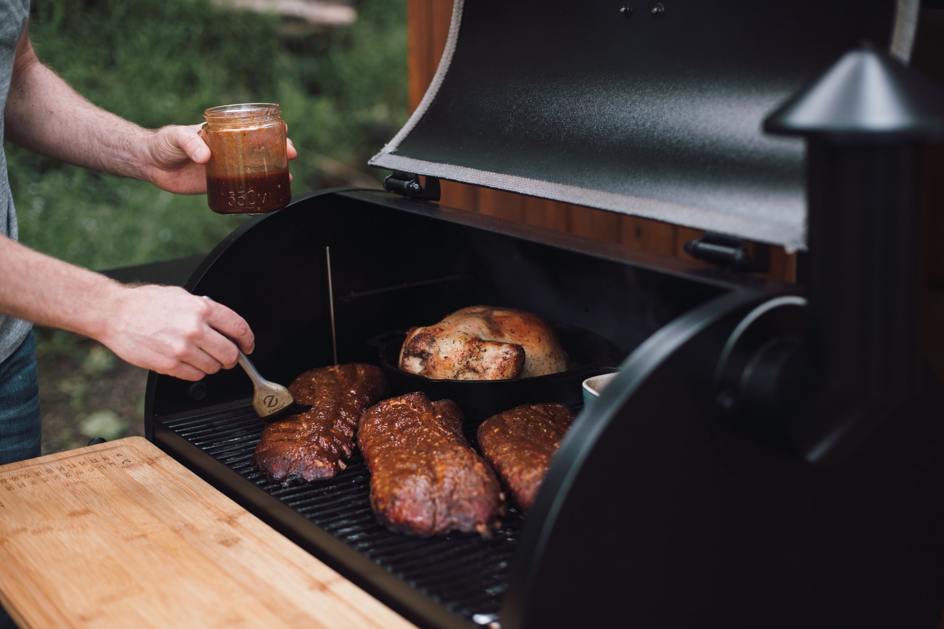 Chefs hands add sauce to meat cooking on one of the best pellet grills for under $500